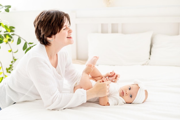 gelukkige familie moeder met baby op bed moeder knuffelt en kust baby dochter moederlijke liefde en zorg moeder met zwangerschapsverlof spelen met baby