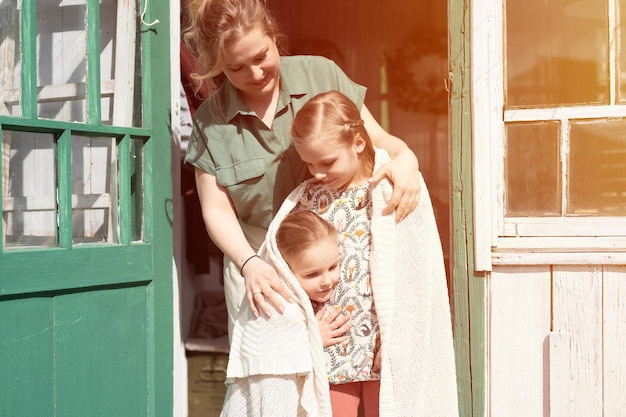 Gelukkige familie moeder met kleine kinderen dochters helper veel plezier op het platteland van de buitenwijken op de wasdag openhartige moeder knuffel en bedek kinderen met plaid en klusjes doen op de veranda van het landhuis flare