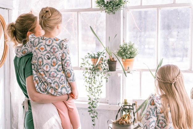 Gelukkige familie moeder met kleine kinderen dochters meisjes hebben plezier in het plattelandsleven van de buitenwijk op zonnige lentedag openhartige moeder en kinderen die bij het raam staan met plant mensen liefde en zorg moment