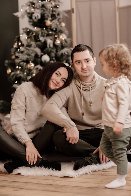 Gelukkige familie, moeder, vader en dochtertje in de buurt van de kerstboom thuis.