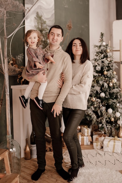 Gelukkige familie, moeder, vader en dochtertje in de buurt van kerstboom en open haard thuis.