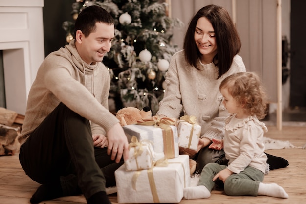 Gelukkige familie, moeder, vader en dochtertje met veel cadeautjes dozen in de buurt van de kerstboom en open haard thuis.