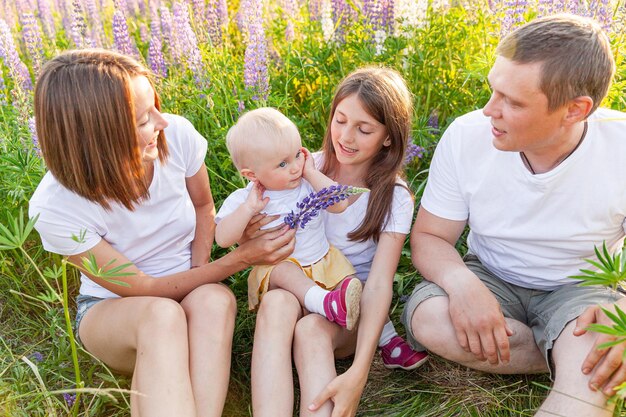 Gelukkige familie moeder vader omarmen kinderen buiten. Vrouw man baby kind en tienermeisje zittend op zomer veld met bloeiende bloemen achtergrond. Gelukkige familie moeder vader en dochters spelen op weide.