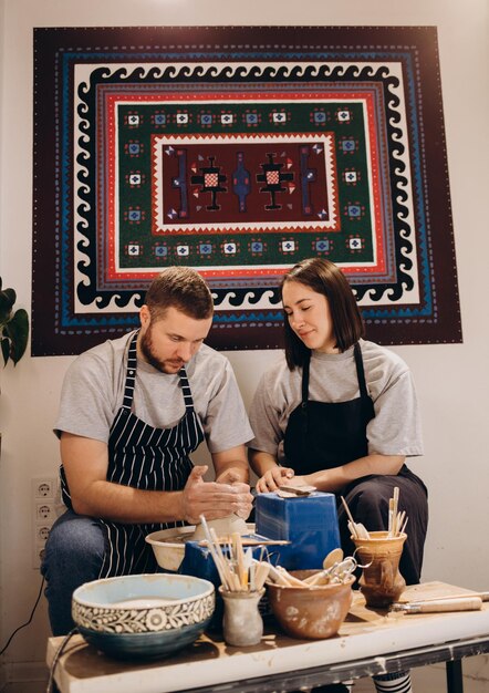 Gelukkige familie op een creatieve gezamenlijke vakantie romantisch verliefd stel werkt samen aan pottenbakkerswiel en beeldhouwt klei pota bebaarde man en een jonge vrouw vormen een vaas in ambachtelijke studio workshop