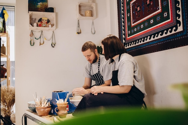 Gelukkige familie op een creatieve gezamenlijke vakantie romantisch verliefd stel werkt samen aan pottenbakkerswiel en beeldhouwt klei pota bebaarde man en een jonge vrouw vormen een vaas in ambachtelijke studio workshop