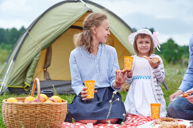 Gelukkige familie op picknick op de camping. Moeder en dochter die dichtbij een tent in weide of park eten