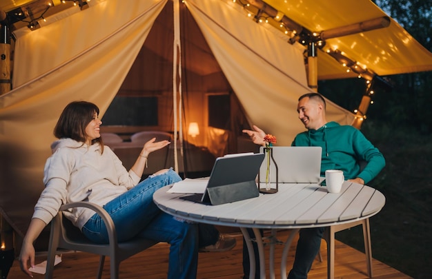 Gelukkige familie paar freelancers hebben een rust na het werken van de laptop op een gezellige glamping tent in de zomeravond luxe camping tent voor buiten vakantie en vakantie lifestyle concept