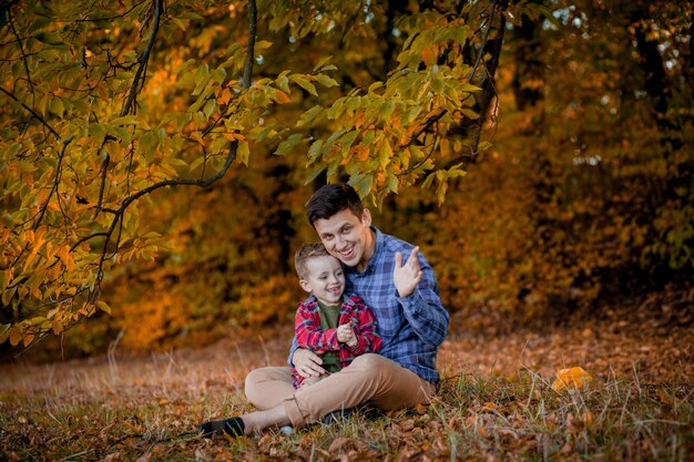 Gelukkige familie plezier buiten in herfst park. Vader en zoon tegen gele vage bladerenachtergrond.