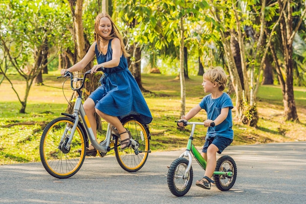 Gelukkige familie rijdt buiten fietsen en glimlacht. Moeder op een fiets en zoon op een loopfiets