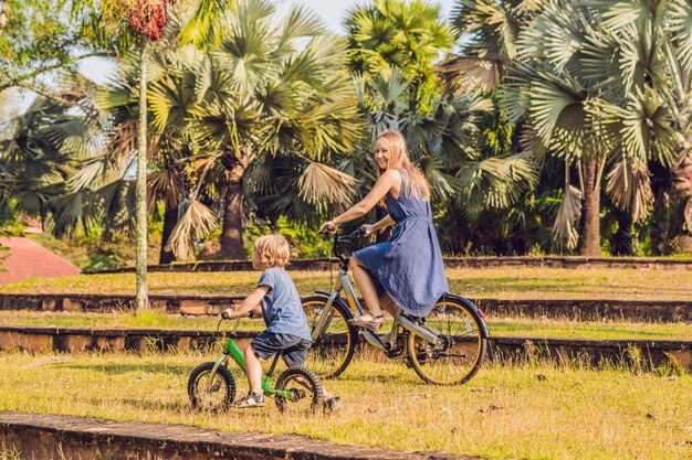 Gelukkige familie rijdt buiten fietsen en glimlacht. Moeder op een fiets en zoon op een loopfiets