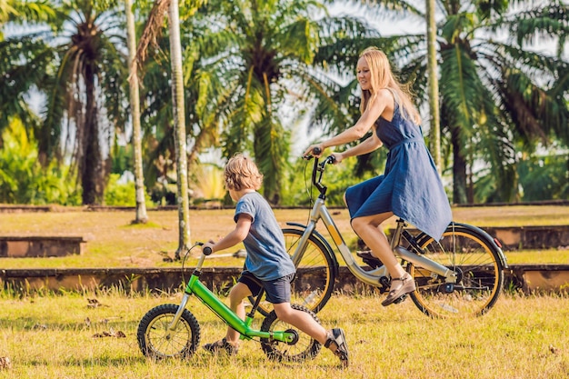 Gelukkige familie rijdt buiten fietsen en glimlacht. Moeder op een fiets en zoon op een loopfiets