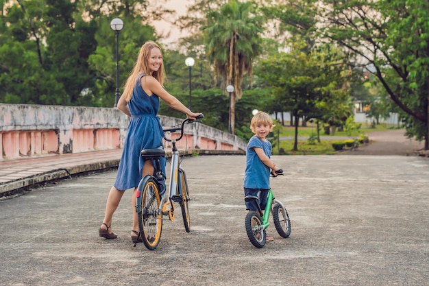 Gelukkige familie rijdt buiten fietsen en glimlacht. Moeder op een fiets en zoon op een loopfiets