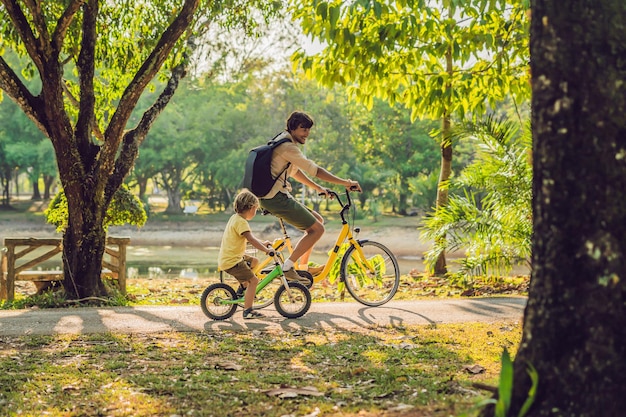 Gelukkige familie rijdt buiten fietsen en glimlacht. Vader op een fiets en zoon op een loopfiets