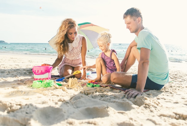 Gelukkige familie spelen op het strand en bouwen een zandkasteel