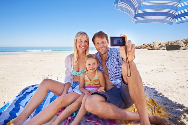Gelukkige familie strand en ontspannen met selfie voor fotografie foto of moment in de natuur buiten moeder vader en kind met glimlach voor foto opname of binding herinnering samen op de oceaan kust