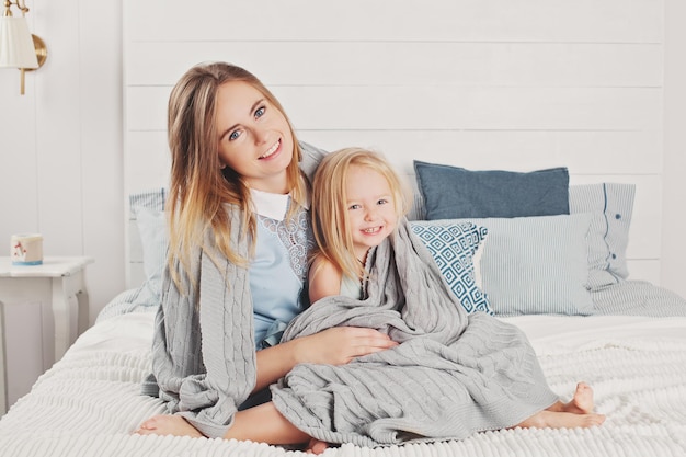 Gelukkige familie thuis aantrekkelijke moeder en kleine dochter zitten op het bed