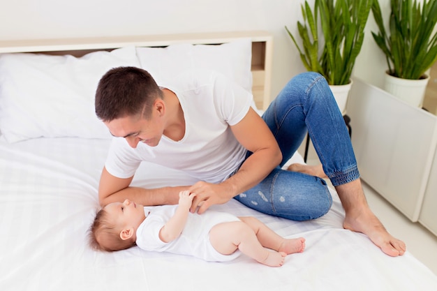 Gelukkige familie: vader en zoon jongen spelen op een wit bed in een zonnige slaapkamer.