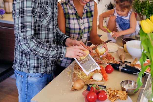 Gelukkige familie van brunette vrouw, knappe man in een fleece shirt en schattig klein meisje koken voedsel in een huis keuken.