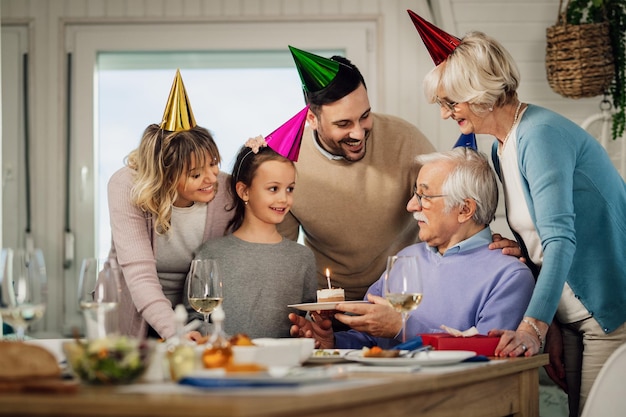 Gelukkige familie van meerdere generaties die de verjaardag van een senior man viert en hem verrast met een verjaardagstaart