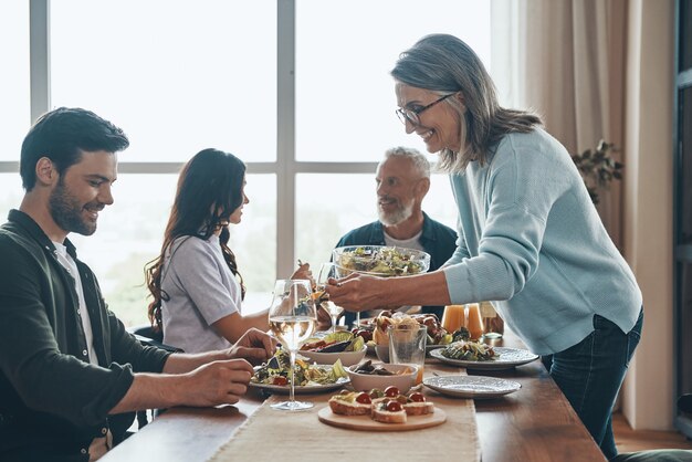 Gelukkige familie van meerdere generaties die geniet van het diner en glimlacht terwijl ze in het moderne appartement zit
