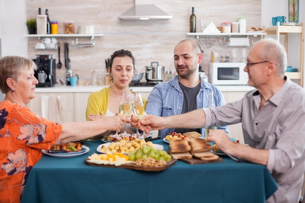 Gelukkige familie van meerdere generaties rammelende wijnglazen tijdens de lunch. Lekkere huisgemaakte gekruide aardappelen. Oudere ouders en oudere kinderen.