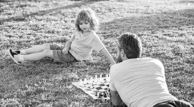 Gelukkige familie van papa en zoon jongen die schaak spelen op groen gras in het park buiten ouderschap