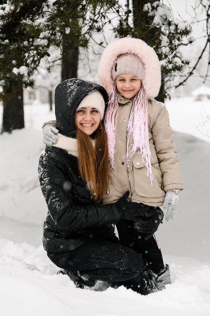 Gelukkige familie veel plezier in het winterbos. Moeder en dochter knuffelen en spelen met sneeuw. Familieconcept. Genieten van tijd samen doorbrengen