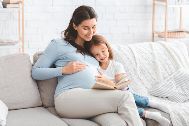 Gelukkige familie zwangere moeder en kleuter dochter tijd samen doorbrengen thuis, boek lezen