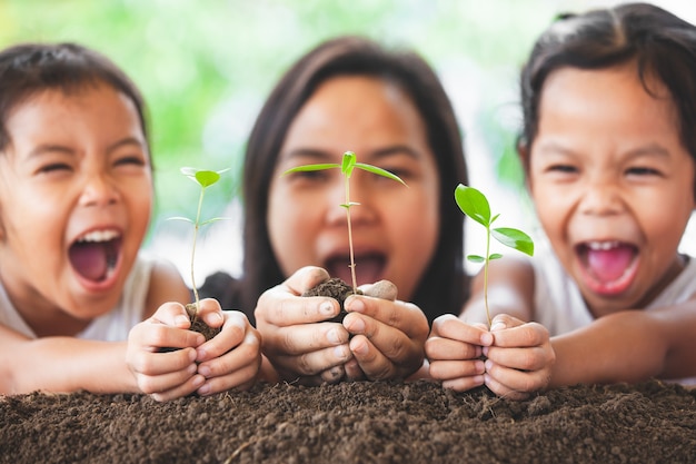 Gelukkige familiemoeder en dochter die pret hebben aan holdings jonge boom in handen voor het planten