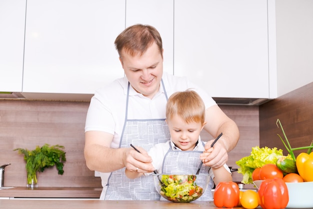 Gelukkige familievader met zoon die groentesalade bij huisgroenten voorbereiden