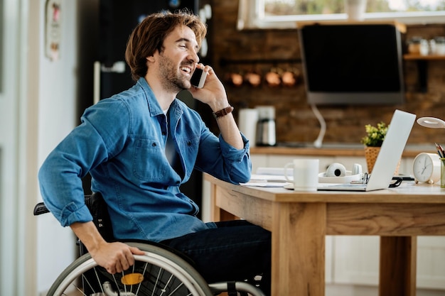 Gelukkige freelancer in rolstoel die via mobiele telefoon communiceert terwijl hij thuis werkt