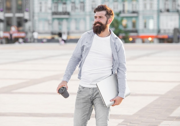 Gelukkige freelancer op straat Freelancer die 's ochtends koffie drinkt Freelancer met een afhaalkop en een laptop Glimlachende freelancer die naar zijn werk gaat