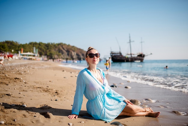 Gelukkige gepensioneerde vrouw met een sjaal die ontspannen op het zand op het strand zit Senior blanke vrouw die buiten op het strand zit