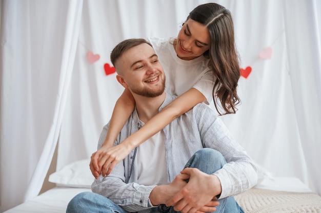 Gelukkige gezichtsuitdrukkingen rode hartvormige decoratie achter jong echtpaar zijn samen thuis