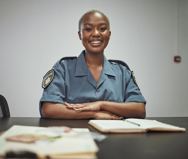 Gelukkige glimlach en portret van een vrouwelijke politieagent die aan een bureau in het kantoor zit en rapporten schrijft Vertrouwen geluk en Afrikaanse vrouwelijke bewaker met een positieve mentaliteit op de werkplek