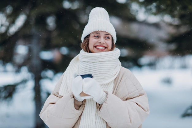 Gelukkige glimlachende jonge vrouw met koffie warme drank beker geniet van het winterweer in het besneeuwde winterpark
