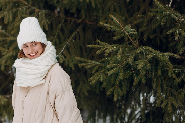 Gelukkige glimlachende jonge vrouw portret gekleed jas sjaal hoed en handschoenen geniet van het winterweer in het winterpark met dennen