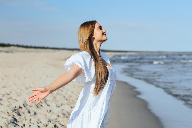 Gelukkige glimlachende mooie vrouw is op het oceaan strand in een witte zomer jurk open armen