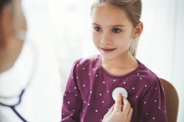 Gelukkige glimlachende patiënt van het kindmeisje bij gebruikelijke medische inspectie. Dokter en kindpatiënt thuis. Geneeskunde, gezondheidszorgconcepten