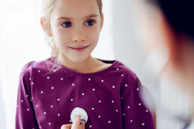 Gelukkige glimlachende patiënt van het kindmeisje bij gebruikelijke medische inspectie. Dokter en kindpatiënt thuis. Geneeskunde, gezondheidszorgconcepten.