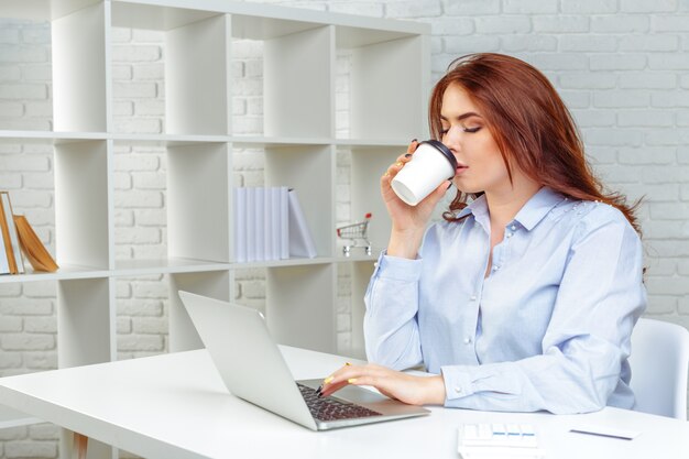 Gelukkige glimlachende vrouw die met laptop werkt en koffie drinkt