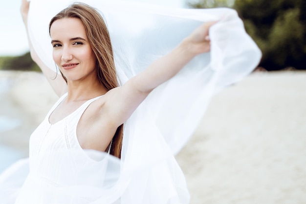 Gelukkige glimlachende vrouw in vrije gelukzaligheid op oceaanstrand dat zich met open handen bevindt. Portret van een multicultureel vrouwelijk model in een witte zomerjurk die geniet van de natuur tijdens vakanties