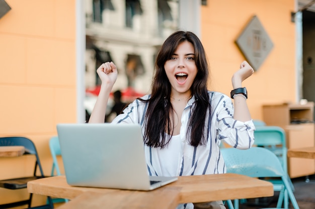 Gelukkige glimlachende vrouw met laptop zitting in openlucht in koffie