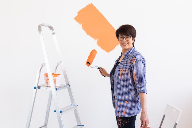 Gelukkige glimlachende vrouw van middelbare leeftijd schilderen binnenmuur van nieuw huis.