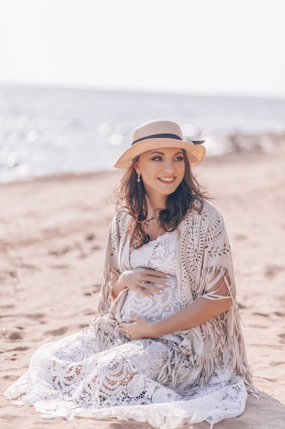 Gelukkige glimlachende zwangere vrouw op het strand