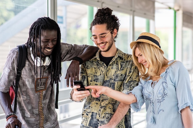 Gelukkige groep vrienden die reizen en wandelen op luchthaven of station multi-etnische mensen genieten van reizen en kijken naar de smartphone voor zoek- en routebeschrijvingen toeristen die technologie gebruiken voor hun reis