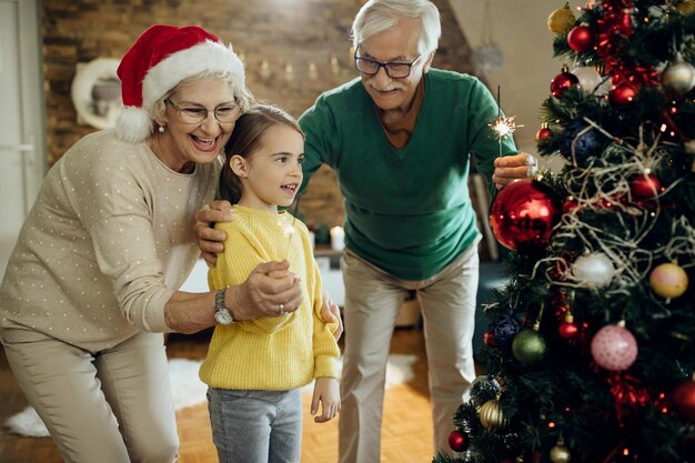 Gelukkige grootouders en hun kleindochter die sterretjes gebruiken terwijl ze thuis Kerstmis vieren