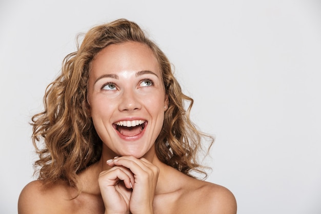 gelukkige halfnaakte vrouw die lacht en naar boven kijkt, geïsoleerd over een witte muur