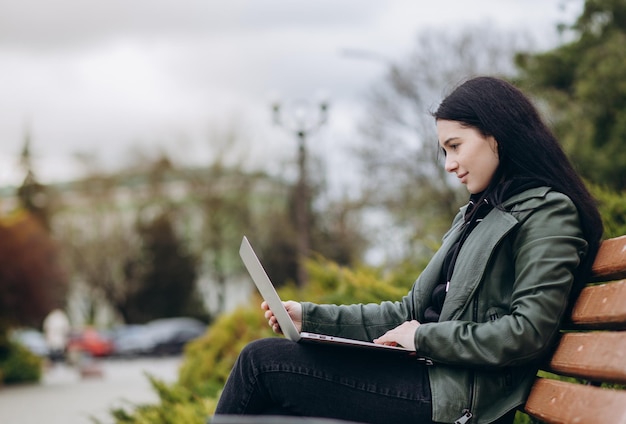 Gelukkige hipster jonge vrouw die aan laptop in het park werkt