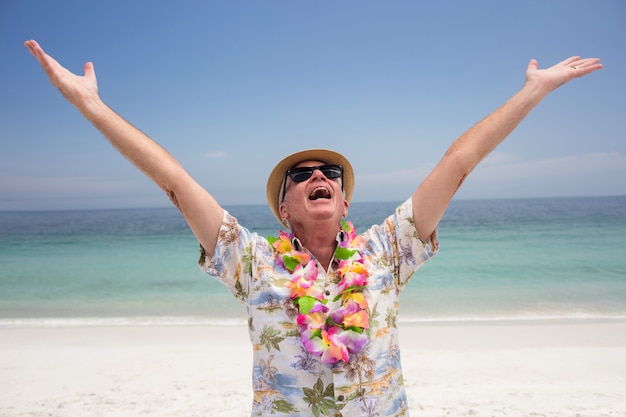 Gelukkige hogere mens die bloemslinger dragen en op het strand genieten van